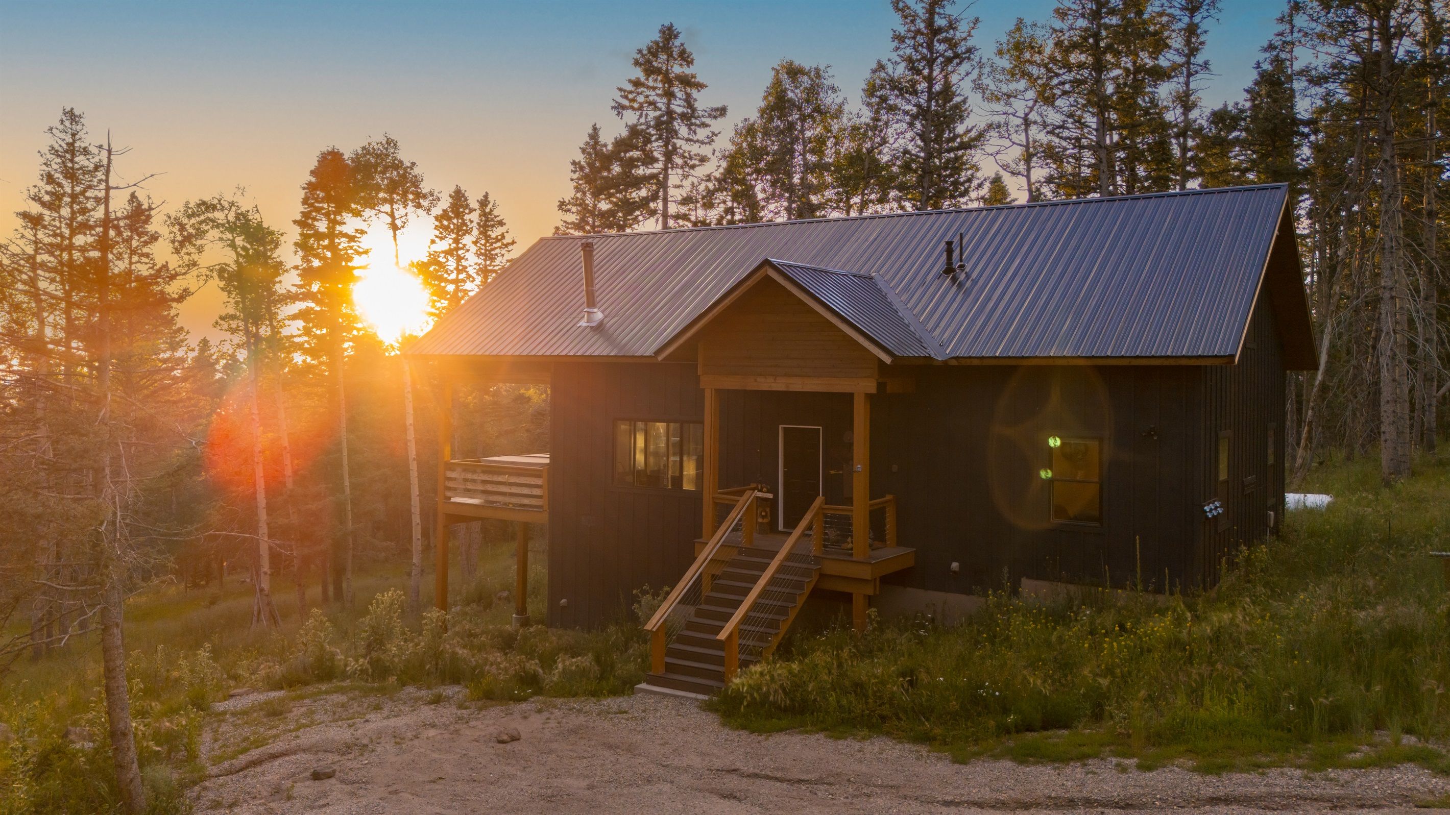 A rustic cabin with a metal roof, wooden deck, and a staircase leading to the entrance.