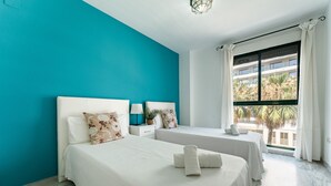 A hotel room with two beds, a teal wall, a large window with a view of palm trees, and a modern light fixture. - MalagaSuite Sky & Sea Torremolinos (Torremolinos)