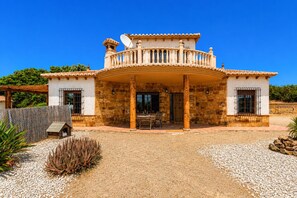 A two-story house with a balcony, stone walls, and a gravel driveway. - MalagaSuite Villa Rural Madeira (Algarrobo)
