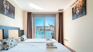 Una habitación de hotel con dos camas, un ventanal con vistas a edificios y obras de arte en las paredes.