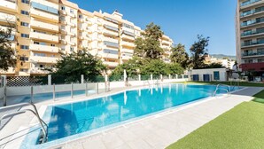 Una piscina con borde de azulejos, rodeada de césped y una valla.
