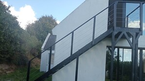 A modern building with a white exterior and black accents, featuring a staircase leading to a balcony.