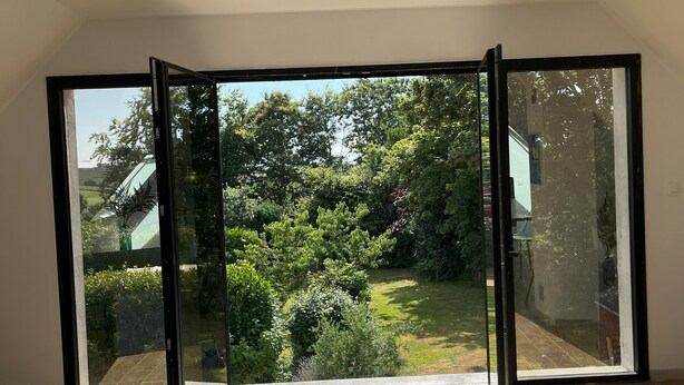 A room with a large sliding glass door leading to a garden with trees and a lawn.