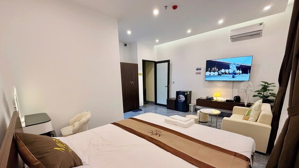 A hotel room with a bed, a desk, a chair, a sofa, a TV, and a small table with a lamp. - Moc Hotel Hung Yen (Nguyen Van Linh)