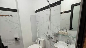 A modern bathroom with a toilet, bidet, and sink, featuring marble walls and a large mirror. - Moc Hotel Hung Yen (Nguyen Van Linh)