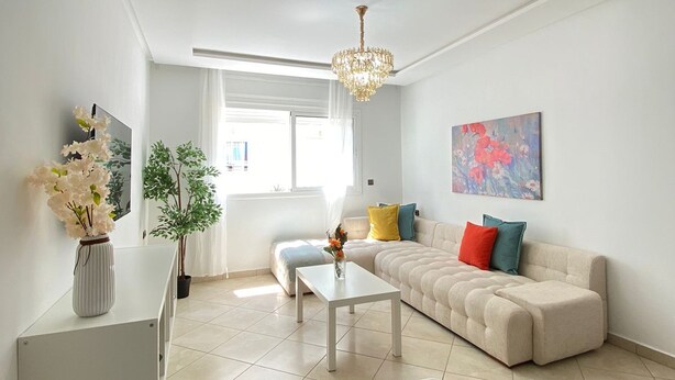 A modern living room with a sofa, a coffee table, a TV, and a chandelier.