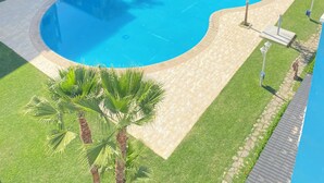A modern hotel with a large swimming pool, surrounded by well-maintained lawns and palm trees.