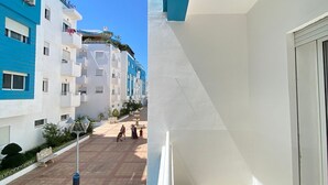 A balcony with a view of a pedestrian street lined with multi-story buildings, some with balconies and plants.
