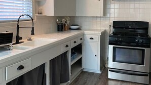 A kitchen with white cabinets, a black stove, and a window with blinds. - Teal Door Rice Village Retreat World Cup dates open (Houston)