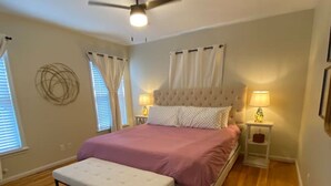 A bedroom with a bed, a bench, a ceiling fan, and two bedside lamps. - Teal Door Rice Village Retreat World Cup dates open (Houston)