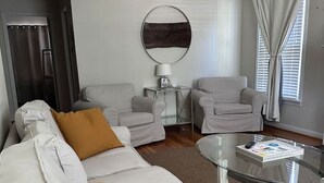 A modern living room with a white sofa, two armchairs, a glass coffee table, and a round wall decoration. - Teal Door Rice Village Retreat World Cup dates open (Houston)