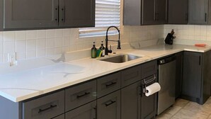 A kitchen with dark cabinets, a white countertop, and a window with blinds. - Rice Village Retreat, World Cup 2026 (Houston)
