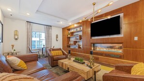 Un salon moderne avec des canapés en cuir, une table basse en bois et un téléviseur à écran plat fixé à un mur en bois.