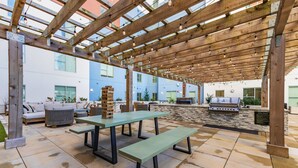 Une terrasse extérieure dotée d’une pergola en bois, de tables, de bancs et d’un barbecue.