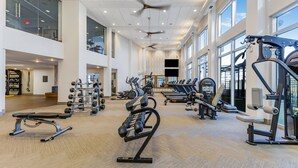 Une salle de sport spacieuse, dotée de divers appareils d’exercice, de grandes fenêtres et d’un plafond haut avec un ventilateur.