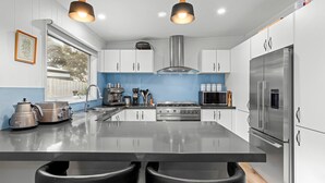 A modern kitchen with white cabinets, stainless steel appliances, and a central island with bar stools. - Lockington Breeze - Point Lonsdale (Point Lonsdale)