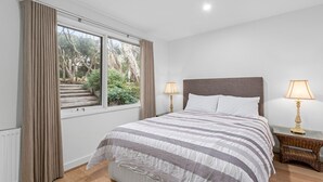 A bedroom with a large bed, two bedside lamps, and a view of a garden through a window. - Lockington Breeze - Point Lonsdale (Point Lonsdale)