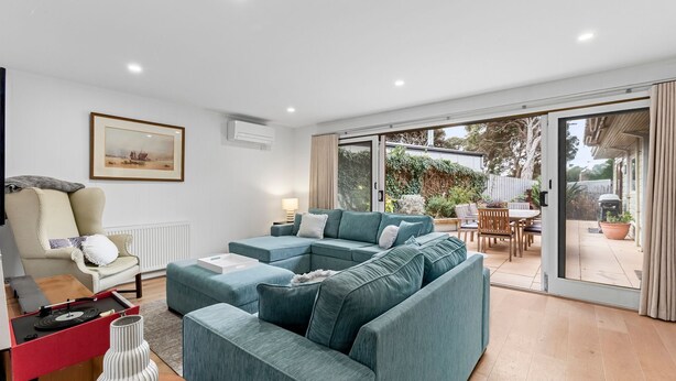 A modern living room with a sectional sofa, a dining area, and a sliding glass door leading to an outdoor space. - Lockington Breeze - Point Lonsdale (Point Lonsdale)