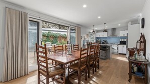 A modern kitchen with white cabinets, a central island, and a dining area with wooden chairs and a table. - Lockington Breeze - Point Lonsdale (Point Lonsdale)