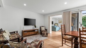 A spacious living room with a flat-screen TV, wooden furniture, and a view into the dining area. - Lockington Breeze - Point Lonsdale (Point Lonsdale)