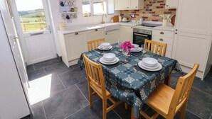 Une cuisine compacte avec des meubles blancs, un mur recouvert de briques et un coin repas aménagé pour quatre personnes, avec une table dressée pour le repas.