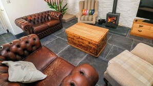 Un salon avec un canapé en cuir marron, un fauteuil à rayures, une table basse en bois et une cheminée en pierre.