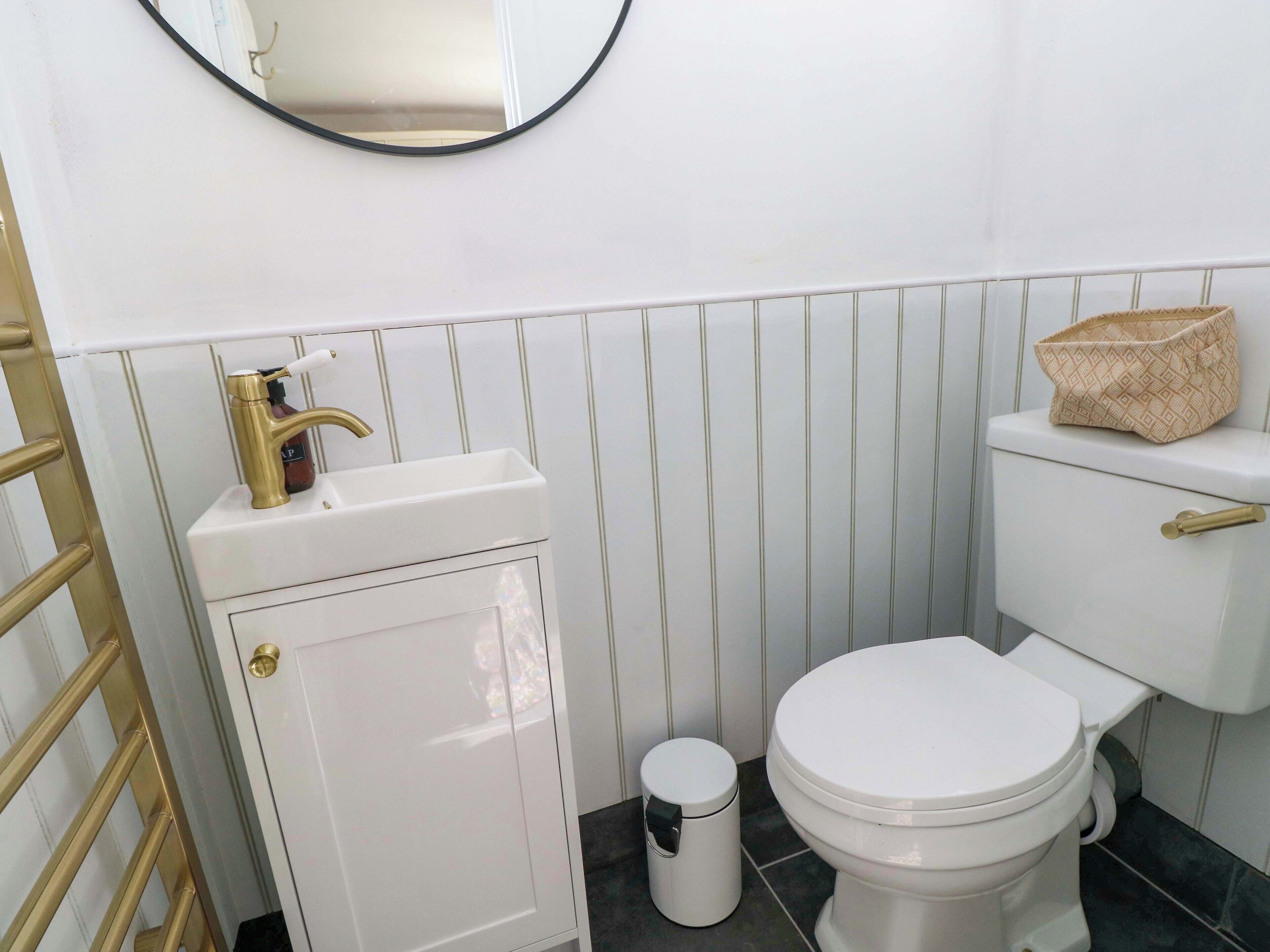 A bathroom with a white sink, gold faucet, and a toilet with a beige basket on the tank.