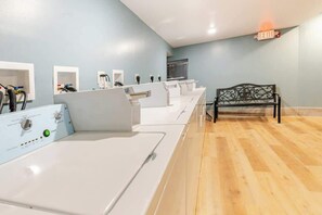 A laundry room with multiple washing machines, a bench, and a wall-mounted exit sign.