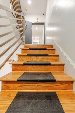 A wooden staircase with a metal railing and a black mat at the bottom.
