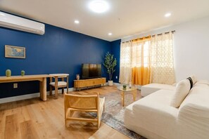 A living room with a sofa, a TV, a wooden table, and a plant.