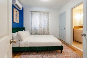 A bedroom with a bed, a green headboard, a patterned curtain, and a door leading to a bathroom.