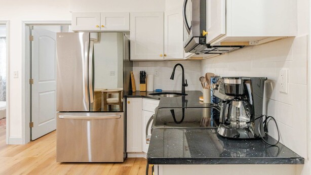 A modern kitchen with stainless steel appliances, white cabinetry, and a black countertop.