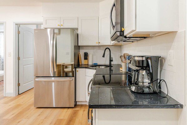 A modern kitchen with stainless steel appliances, white cabinetry, and a black countertop.
