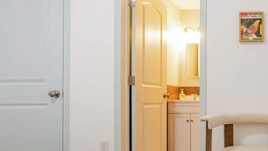 A bedroom with a bed and a chair, a hallway leading to a bathroom with a sink and mirror, and a door leading to another room.