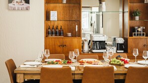 A dining area with a wooden table set for a meal, surrounded by chairs. There are bottles and a sign on the wall, and a kitchen area is visible in the background. - Pinch of Cozy ~ Hot Tub Theater ~ Seven Sons Farm (Roanoke)