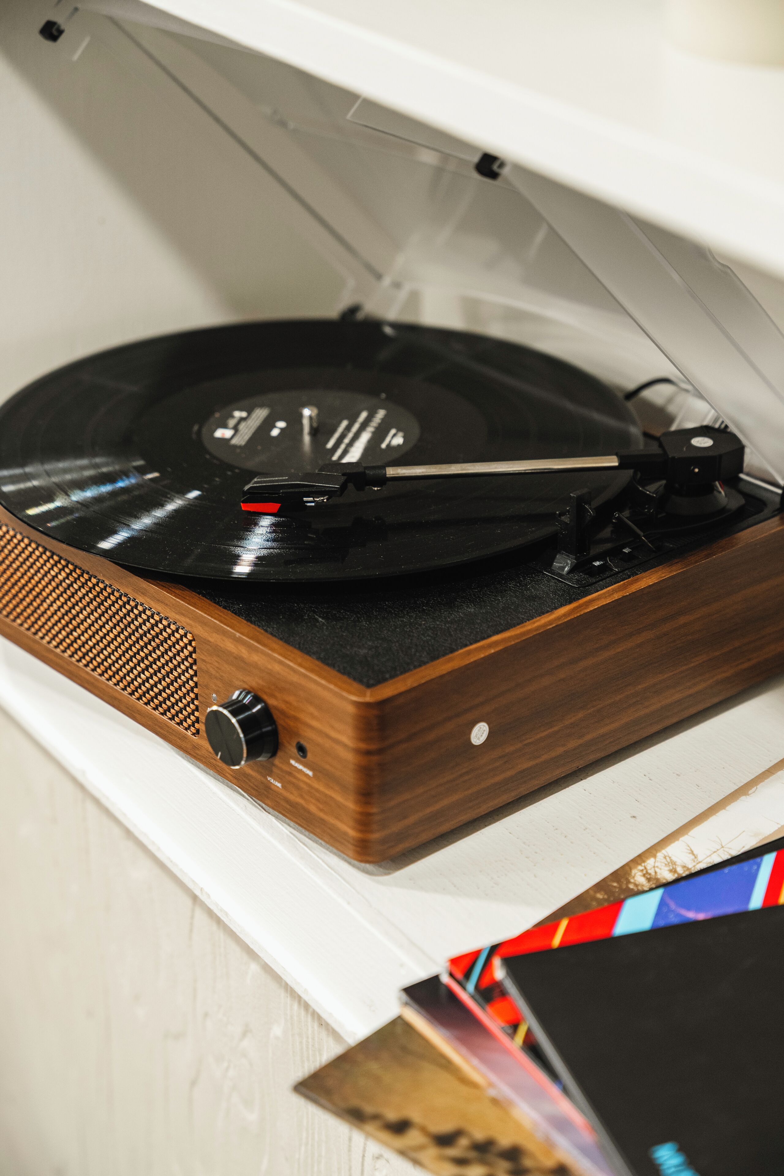 Une platine vinyle dotée d’un socle en bois et d’un couvercle transparent, posée sur une surface blanche.