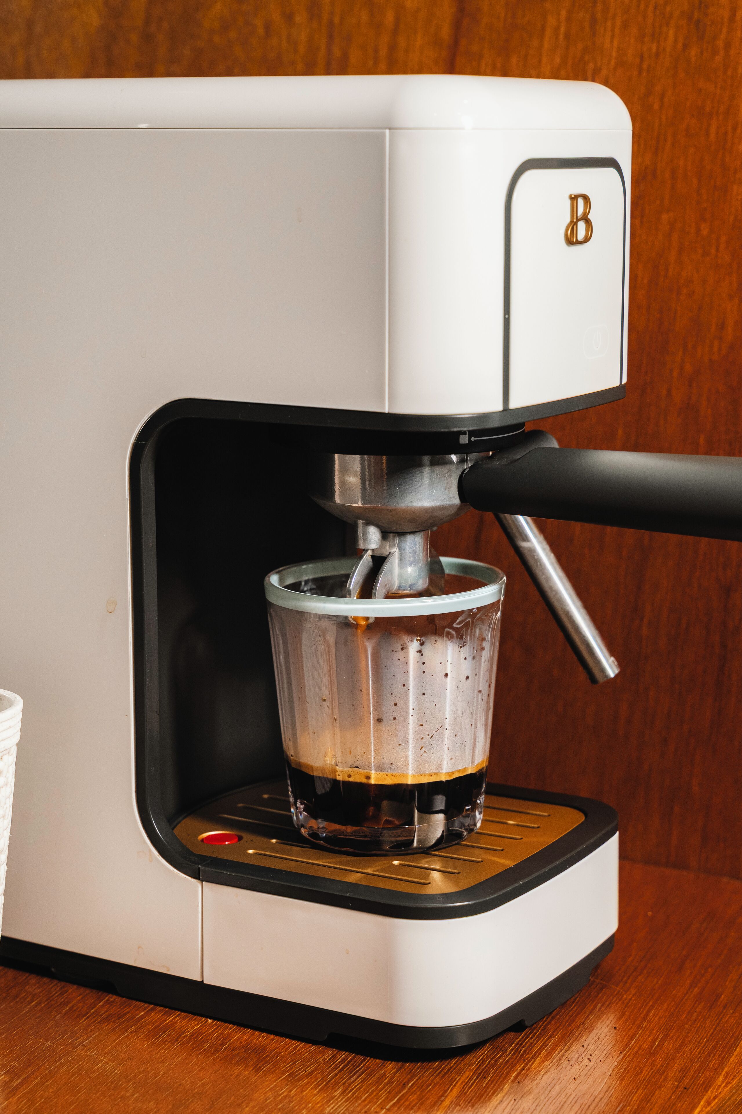 Màquina de cafè amb un recipient de vidre i un filtre metàl·lic, damunt d'una superfície de fusta.