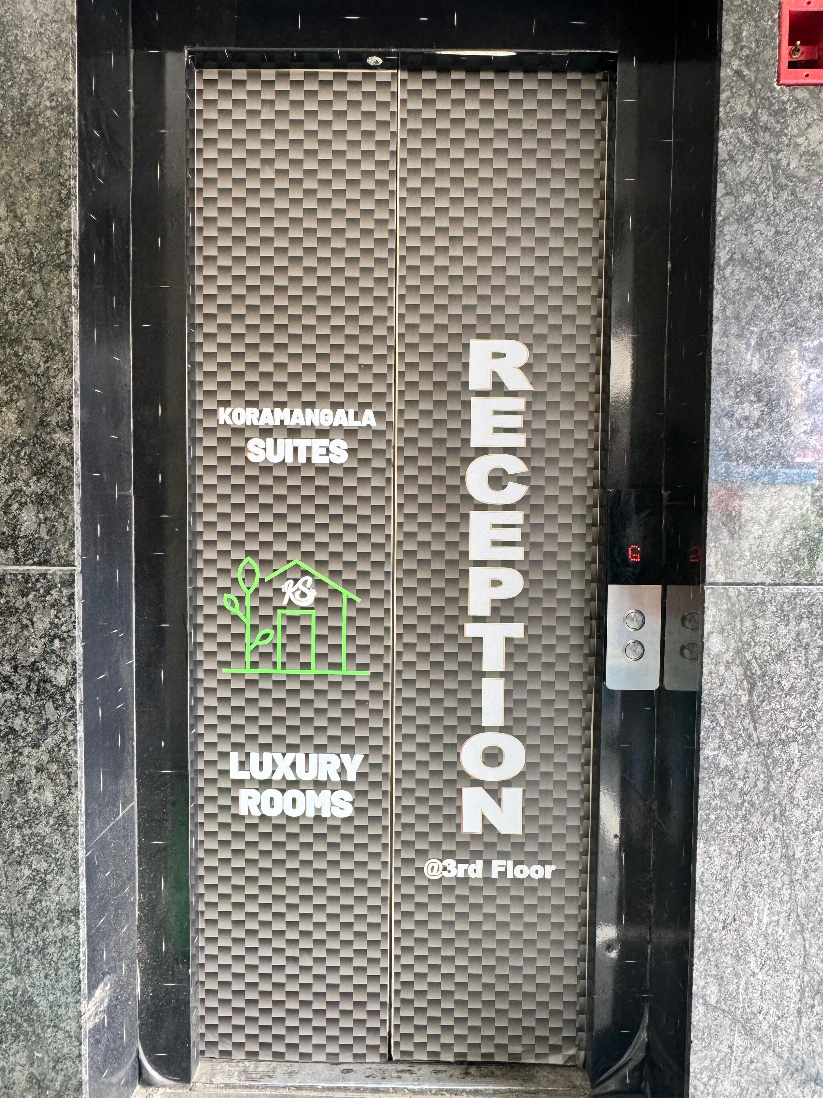 An elevator door with "RECEPTION" and "KORAMANGALA SUITES LUXURY ROOMS @3rd Floor" signage.