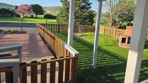 A covered outdoor area with a wooden fence, a brick structure, and a view of a green landscape.