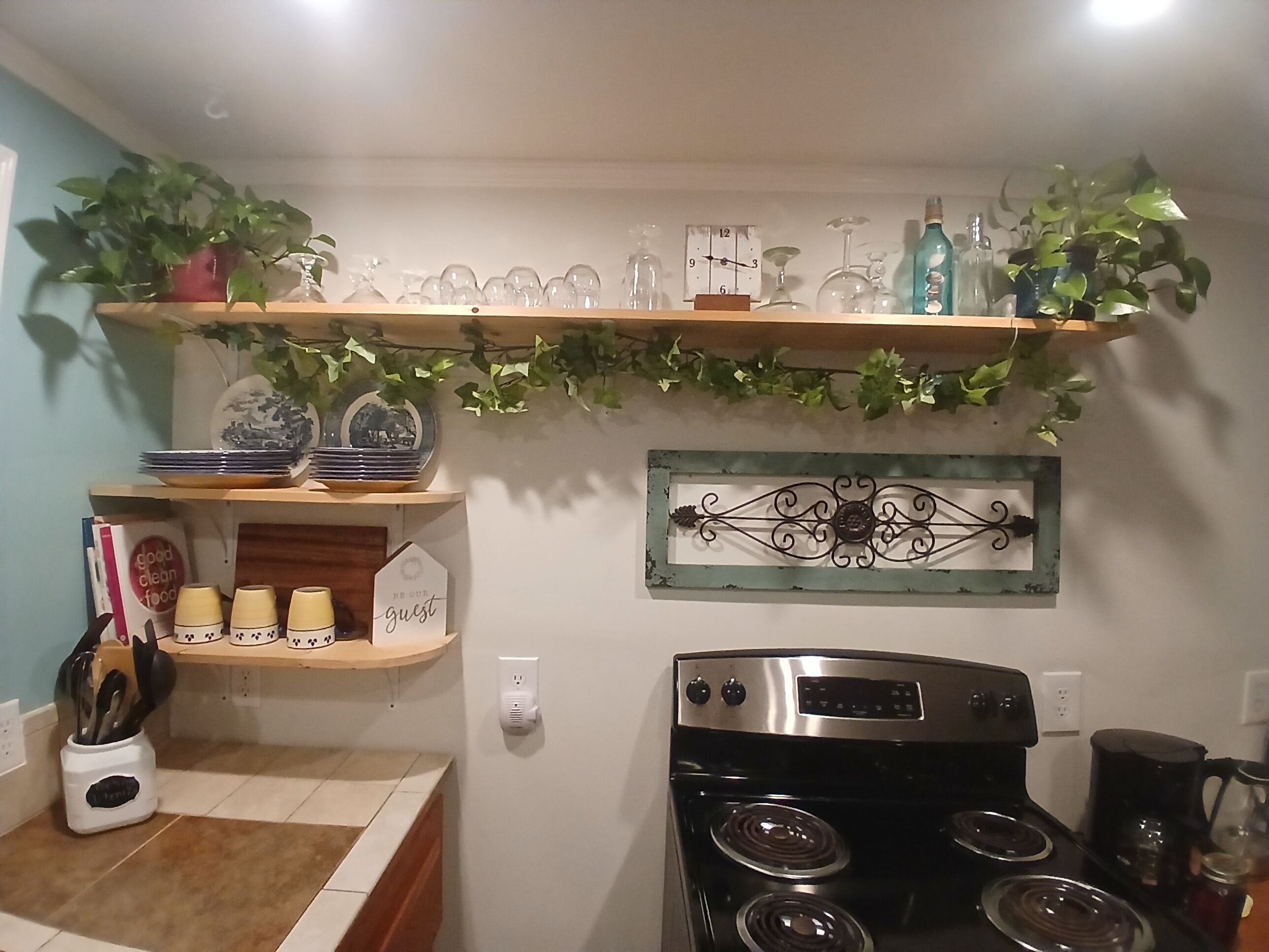 Une cuisine équipée d’une cuisinière, de rayonnages où sont rangés des verres, et d’un élément décoratif en métal accroché au mur.