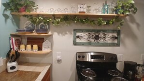 A kitchen with a stove, shelves with glassware, and a decorative metal piece on the wall.