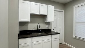 A kitchen with white cabinets, a black countertop, and a window with blinds. - Cozy 2-bedroom apartment Near Six Flags & Attractions (Springfield)