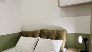 A neatly made bed with white linens, a brown headboard, and a bedside lamp.