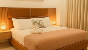 A neatly made bed with a brown headboard, white bedding, and decorative pillows. There are two bedside lamps on either side of the bed.