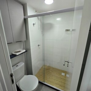A modern bathroom with a glass-enclosed shower, a toilet, and a shelf with towels. - legacy 417 - Cabo Branco (João Pessoa)