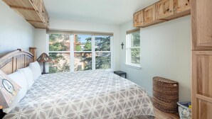 Ein Schlafzimmer mit einem großen Bett, Holzschränken, einem Fenster mit Ausblick und einem Korbwäschekorb.
