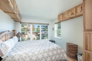 Une chambre avec un grand lit, des armoires en bois, une fenêtre donnant sur un beau paysage et un panier en osier.
