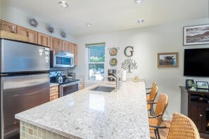 A modern kitchen with granite countertops, stainless steel appliances, and a dining area with wicker chairs.