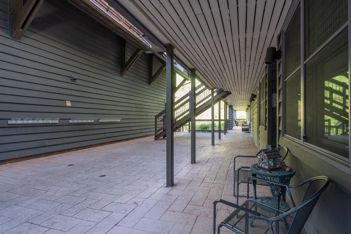 A covered walkway with a tiled floor, metal chairs, and a decorative table.