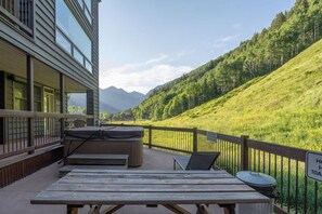 A wooden deck with picnic tables and a barbecue grill, overlooking a forested hillside.